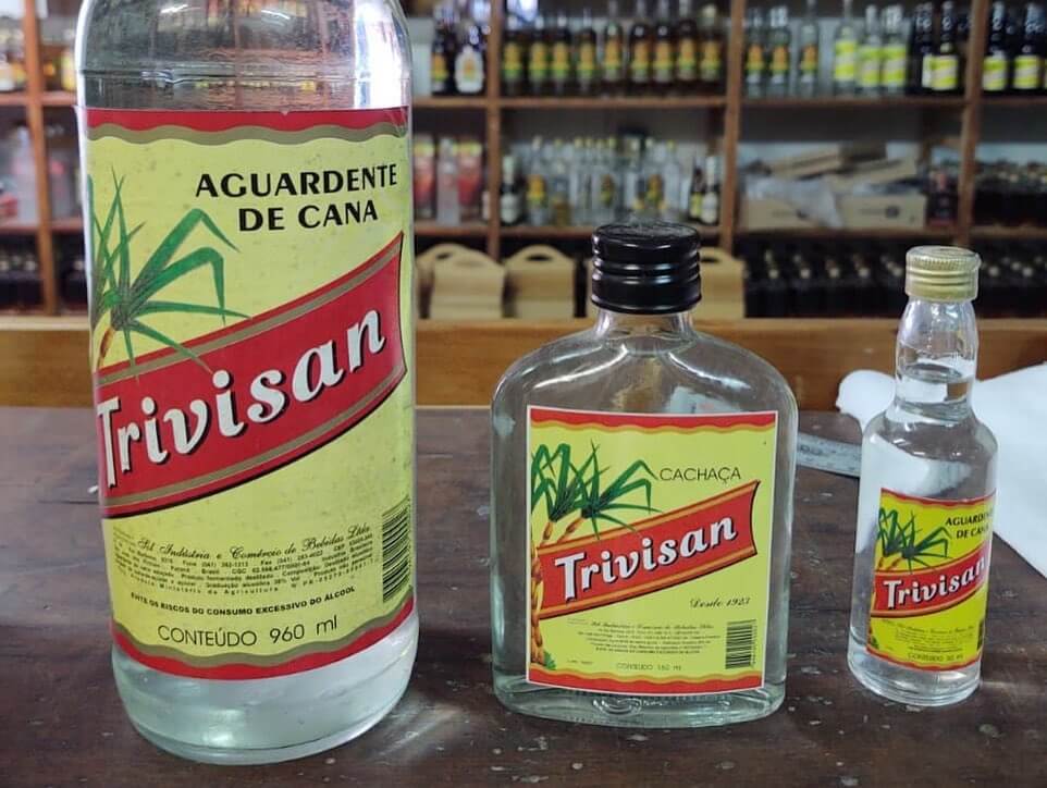 Três garrafas com rótulo atual em amarelo e vermelho da cachaça Trevisan