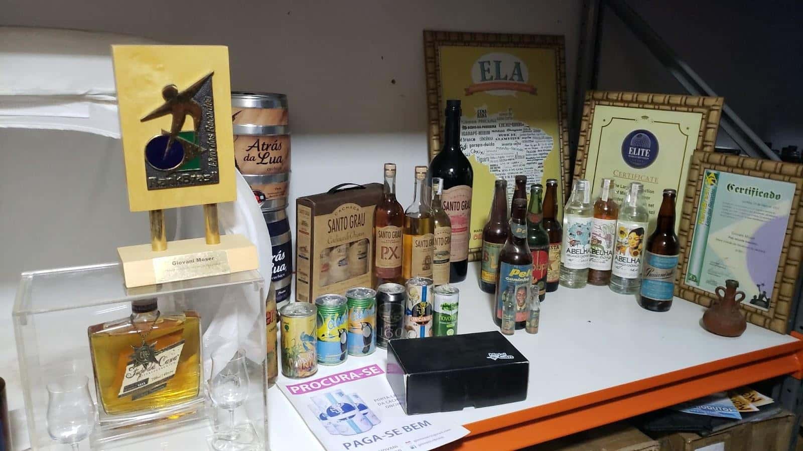 Mesa com diversas garrafas, quadros e outros item de colecionador de cachaças